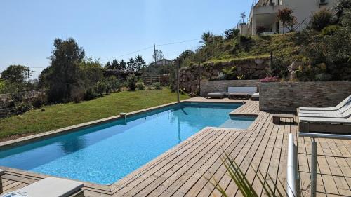 une piscine avec une terrasse en bois et une maison dans l'établissement Superbe villa moderne sur Capo di Muro, à Coti-Chiavari