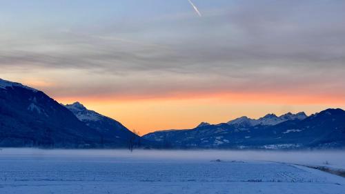 a view of a snow covered mountain range with the sun setting at Binter Haus -Rattendorf in Rattendorf