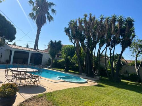 a patio with a table and chairs and palm trees at Appartement avec piscine et barbecue in La Farlède