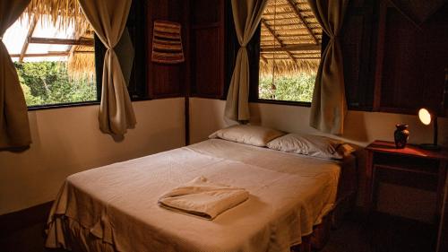 a bed in a room with two windows at Casa Muiraquitã Experiências Amazônicas in Santarém