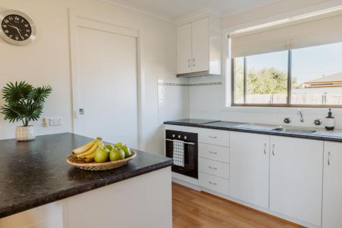 a kitchen with white cabinets and a bowl of fruit on a counter at The Seaside Spot in Devonport