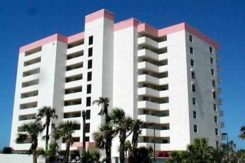 un grand bâtiment blanc avec des palmiers devant dans l'établissement Direct oceanfront corner condo with spacious balcony and heated beachfront pool, à Ormond Beach