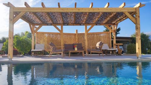 a pergola with chairs and a table next to a pool at Stonehouse Olivelia - Afrathias Beach in Tympáki