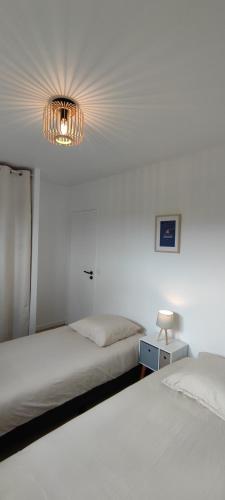 a white bedroom with two beds and a chandelier at Ti vakansin war aod an emrodez in Ruca