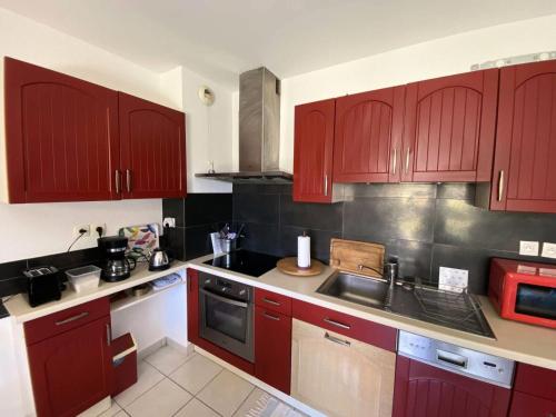 une cuisine avec des armoires rouges et un évier dans l'établissement Résidence Les Vagues - 156 - Appartement en rez de jardin résidence Les Vagues MAE-7381, à Soulac-sur-Mer