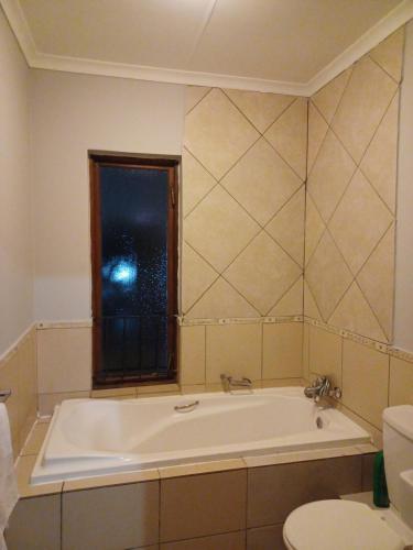 a bathroom with a tub and a toilet and a window at Sanctuary at Waterfall in Midrand