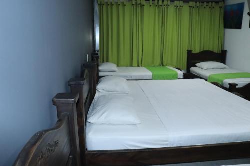 three beds in a room with a green curtain at Hotel Inambu Villavicencio in Villavicencio