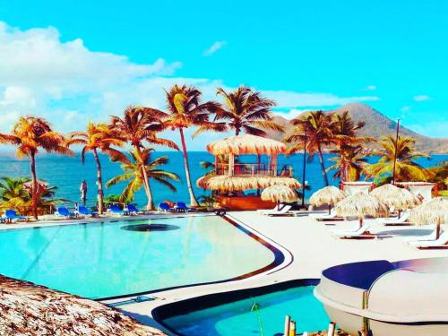 a swimming pool with palm trees and the ocean at 412 The Diamond Swing in Le Diamant