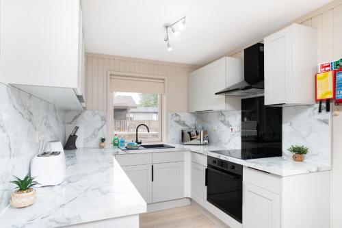 a white kitchen with white cabinets and black appliances at Lodge -3 Bedrooms - Hunters Quay in Kilmun