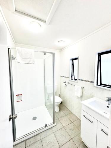 a white bathroom with a shower and a toilet at Papakura Pioneer Motor Lodge & Motel in Papakura