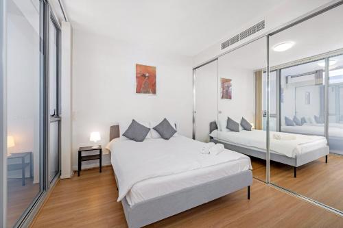 a white bedroom with two beds and a mirror at Modern 2BR Apartment in Sydney