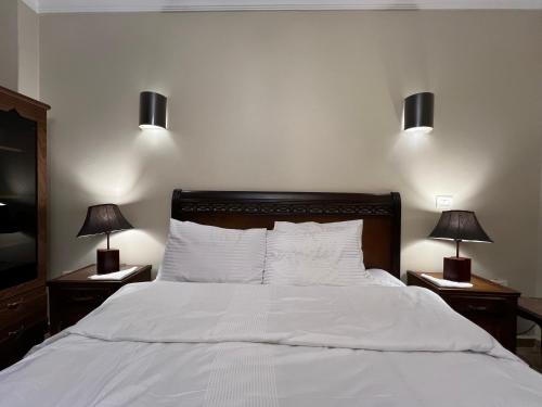 a bedroom with a white bed with two lamps at Luxury apartment in private compound in New Cairo in Banī Ghālib