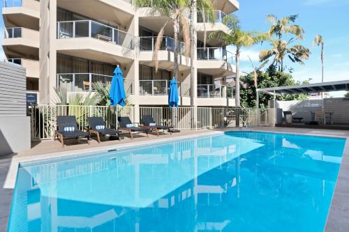 a swimming pool in front of a building with blue umbrellas at The Sebel Sydney Manly Beach in Sydney