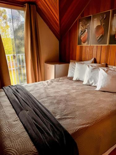 a bedroom with a large bed with a window at Pousada Araucária Suítes in Campos do Jordão