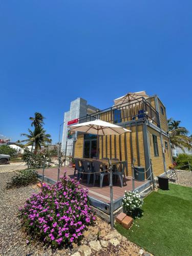a patio with an umbrella and flowers in front of a building at Yellow house 6 minutos de playa in Barra de Navidad
