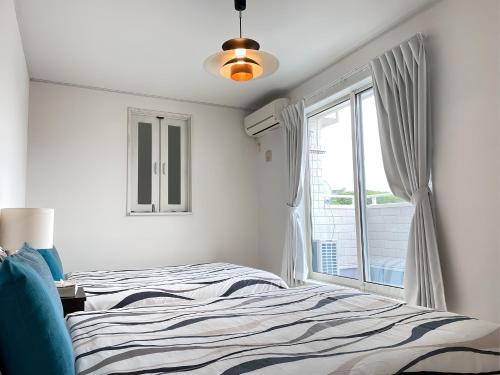 a white bedroom with a bed and a window at 美ら海水族館まで車で5分 ジャングリアにも車で25分の好立地 Villa Clownfish Reef in Motobu