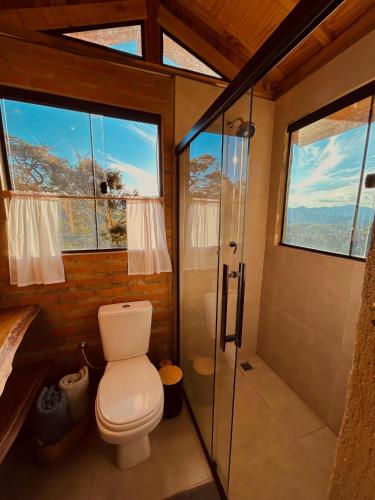 a bathroom with a toilet and a shower with windows at Cabana Serra do Vento in Passa Quatro