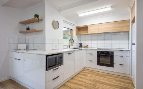 a white kitchen with wooden floors and white cabinets at Middleton Beach Holiday Apartment in Albany