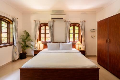 a bedroom with a large bed with two windows at Beachside Bliss Villas Candolim 10 min walk from Sinquerim Beach in Sinquerim
