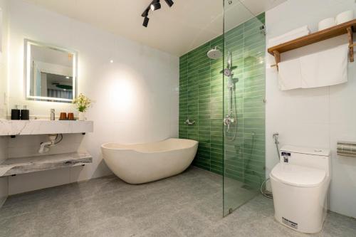 a bathroom with a tub and a toilet and green tiles at Greenfield Village Home in Hoi An