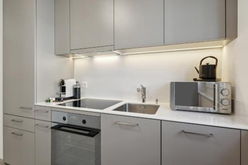 a white kitchen with a sink and a microwave at UP&GREAT Apartments - Stylish City Living in Zürich