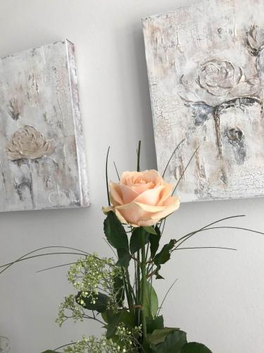 a pink rose in a vase next to two paintings at Sylter Rose in Süderende