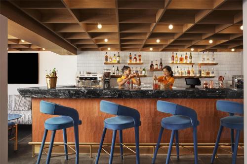 two women standing at a bar with blue stools at Hyatt Ronil Goa - a JdV by Hyatt Hotel in Calangute