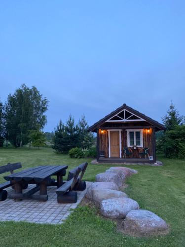 a cabin with a picnic table and benches in a field at Cozy chalet for nature lovers in Ķevele