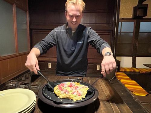 a man is cooking food in a pan on a table at 古民家一棟貸しナノビレッジ岡山 in Kaga