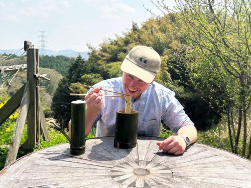 a man sitting at a table with chopsticks in a cup at 古民家一棟貸しナノビレッジ岡山 in Kaga