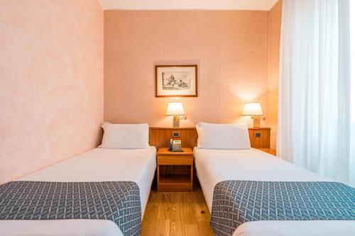 a room with two beds and a desk with two lamps at Crystal Hotel Varese in Varese