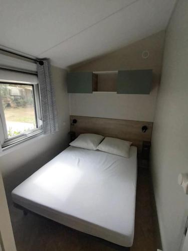 Cette petite chambre dispose d'un lit blanc et d'une fenêtre. dans l'établissement Mobil home prémium 8 pers camping 4 étoiles, à Saint-Cyprien