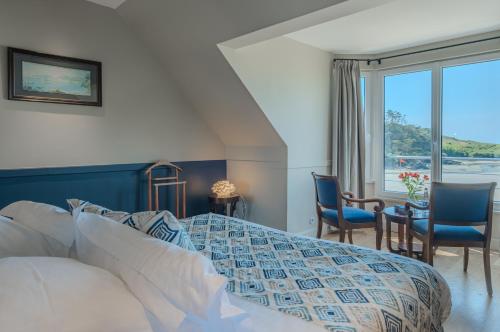 a bedroom with a bed and chairs and a window at Hôtel de la Plage in Plonévez-Porzay