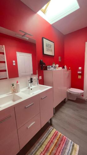 La salle de bains est pourvue de murs rouges, d'un lavabo et de toilettes. dans l'établissement Maison indépendante en centre ville, au Mans