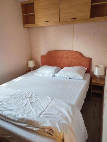 un lit avec des draps blancs et des oreillers dans une chambre dans l'établissement Mobil Home 3 chambres au Camping Paradis du Quinquis, à Clohars-Carnoët