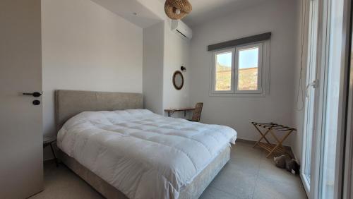 a white bedroom with a large bed and a window at Vista del sole Kythnos in Kithnos
