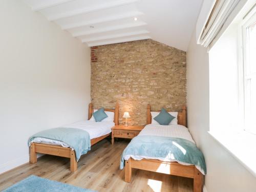 2 letti in una camera con muro di mattoni di South Barn Cottage a Faringdon