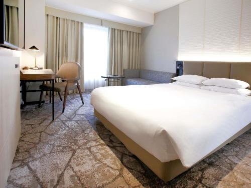 una camera con un grande letto bianco e una scrivania di The Cypress Mercure Hotel Nagoya a Nagoya