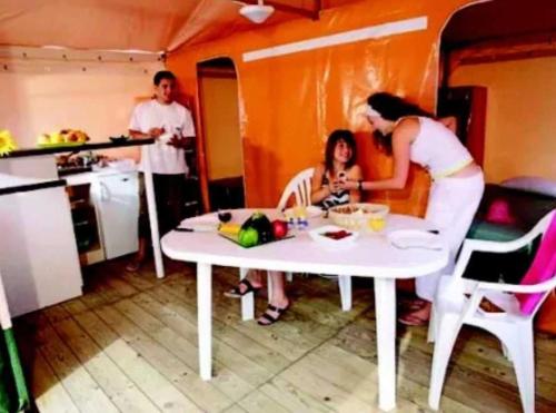 a woman sitting at a white table in a kitchen at Camping 3 étoiles - ccaiaah in Monoblet