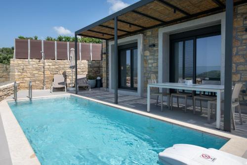 a house with a swimming pool and a table at Porti Villas Aphrodite in Asómatoi