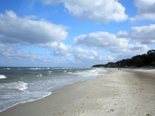 Una playa con gente caminando sobre la arena y el océano. en Peenemünde, Seglerhafen_SB_Slup 12 15, en Peenemünde