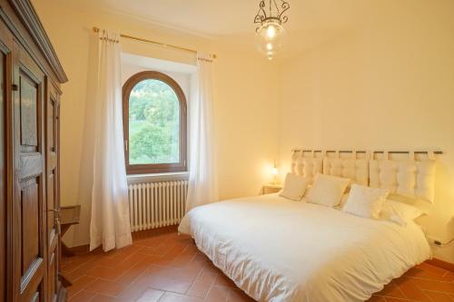 Un dormitorio con una gran cama blanca con ventana. en Tenuta d'Elci - Relax e Piscina nel Bosco, en Casteldelci