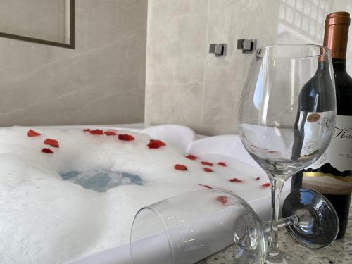 a wine glass sitting next to a bath tub with red pedals at Pousada Maria Monteiro Tiradentes in Tiradentes