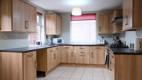 a kitchen with wooden cabinets and a black counter top at Lovely 5 Bedroom Home w Garden near Northampton in Earls Barton