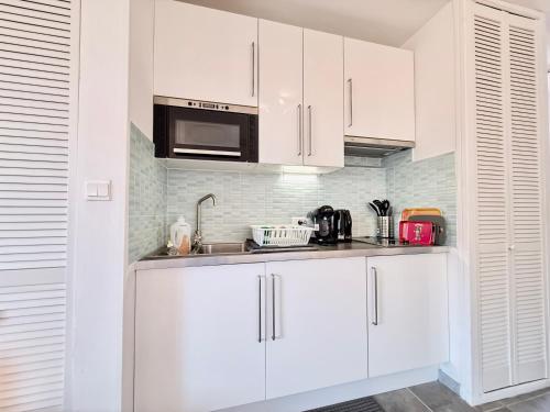 une cuisine blanche avec un évier et un micro-ondes dans l'établissement Studio Moderne - Terrasse - Parking Privé, à Carqueiranne