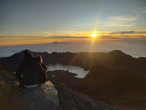 a person sitting on top of a mountain watching the sunset at Iza home stay in Senaru