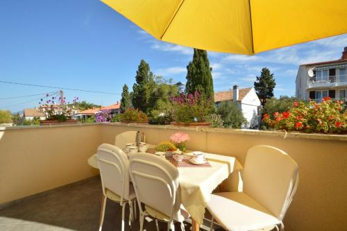 a table and chairs on a balcony with a yellow umbrella at House Orhideja in Mali Lošinj