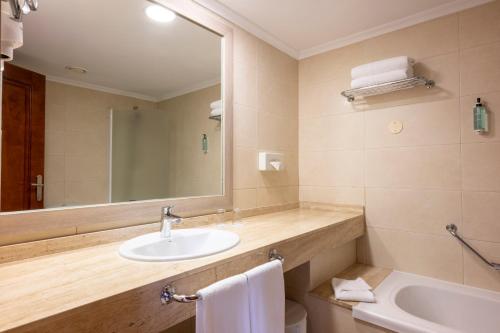 a bathroom with a sink and a mirror and a toilet at Landmar Costa los Gigantes Family Resort in Puerto de Santiago