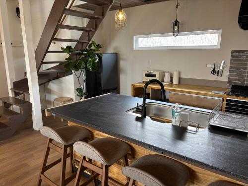 a kitchen with a sink and a counter with stools at 簡易宿所 51ハウス 音と温泉 みんなで時間を楽しむ貸切一軒家 in Shiraoi