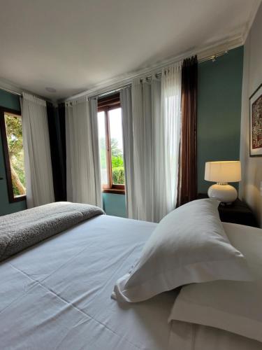 a bedroom with a large white bed with windows at Espaço Tramonto in Itaipava